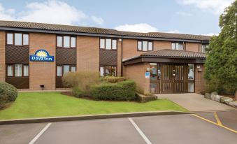 a days inn hotel with a brown and white facade , surrounded by green grass and trees at Days Inn by Wyndham Sedgemoor M5