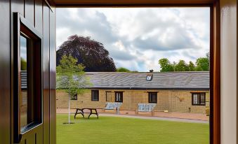 a view of a brick building and a green lawn with two benches , one of which is covered at Church Farm Lodge