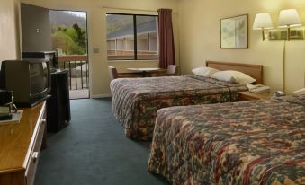 a hotel room with two beds , a television , and a balcony door , all decorated in warm colors at Americas Best Value Inn Canton