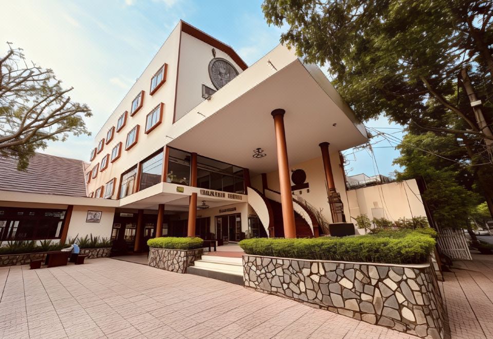 a modern building with a stone facade and white columns , surrounded by trees and bushes at DAM San Hotel