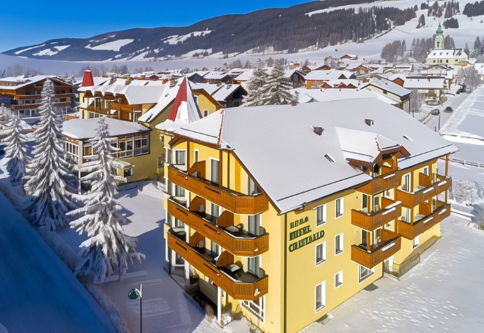 a large hotel surrounded by snow - covered mountains , with a blue sky in the background at Hotel Cristallo