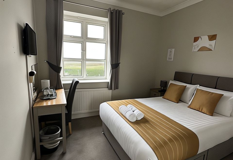 a neatly made bed with a gold blanket and white pillows is in a room with a window at Rettendon Lodge