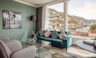 a modern living room with a blue couch , glass coffee table , and large windows overlooking the city at Clarion Hotel Bergen