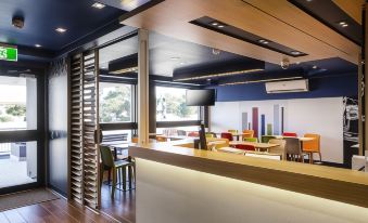 a modern restaurant with wooden tables , chairs , and a bar , as well as a large window allowing natural light to enter at Ibis Budget Windsor Brisbane