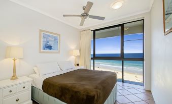 a bedroom with a large bed , white walls , and a view of the beach through a window at Coolum Caprice