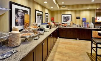 a dining area with a buffet table filled with various food items and utensils , including bowls , cups , spoons , and forks at Hampton Inn Ashland