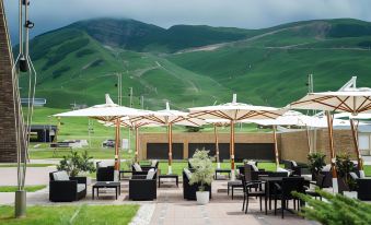 a patio area with several tables and chairs , surrounded by a lush green field and mountains in the background at Shahdag Hotel & Spa