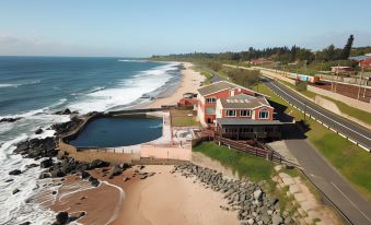 a large house is situated on a beach with a walkway leading to the ocean at Umkomaas Lodge