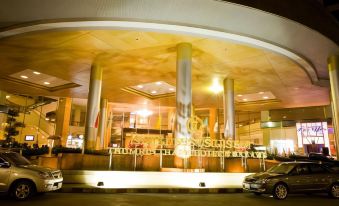 a hotel entrance with a large gold sign and pillars , along with a car parked nearby at Thumrin Thana Hotel