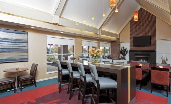 a modern restaurant with a bar and dining area , featuring blue chairs and a red rug at Residence Inn Lansing West