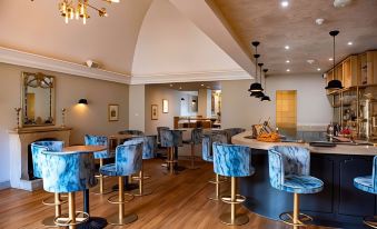 a dining room with wooden floors , blue chairs and tables , and a large chandelier hanging from the ceiling at The Haycock Manor Hotel