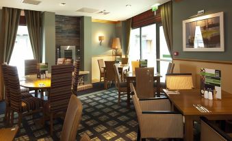 a dining room with wooden tables and chairs arranged for a group of people to enjoy a meal together at Premier Inn Newquay (Quintrell Downs)