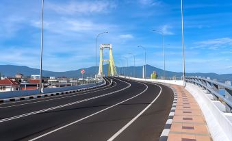a long , empty road with a yellow bridge in the background and mountains in the background at RedDoorz Plus @ Paal 2 Manado