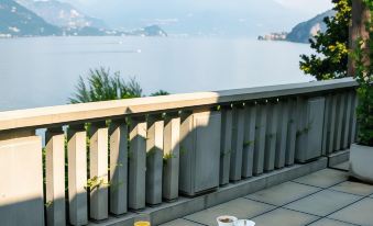 a table with breakfast items is set on a balcony overlooking a lake and mountains at Villa Lario Resort Mandello