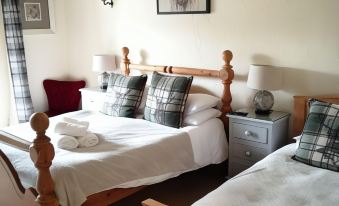 a cozy bedroom with two wooden beds , white bedding , and plaid pillows , along with a cow painting on the wall at The Brown Horse Inn