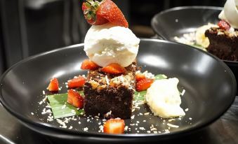 a black plate with a chocolate cake topped with whipped cream and strawberries , accompanied by a bowl of strawberries at Cairns Colonial Club Resort