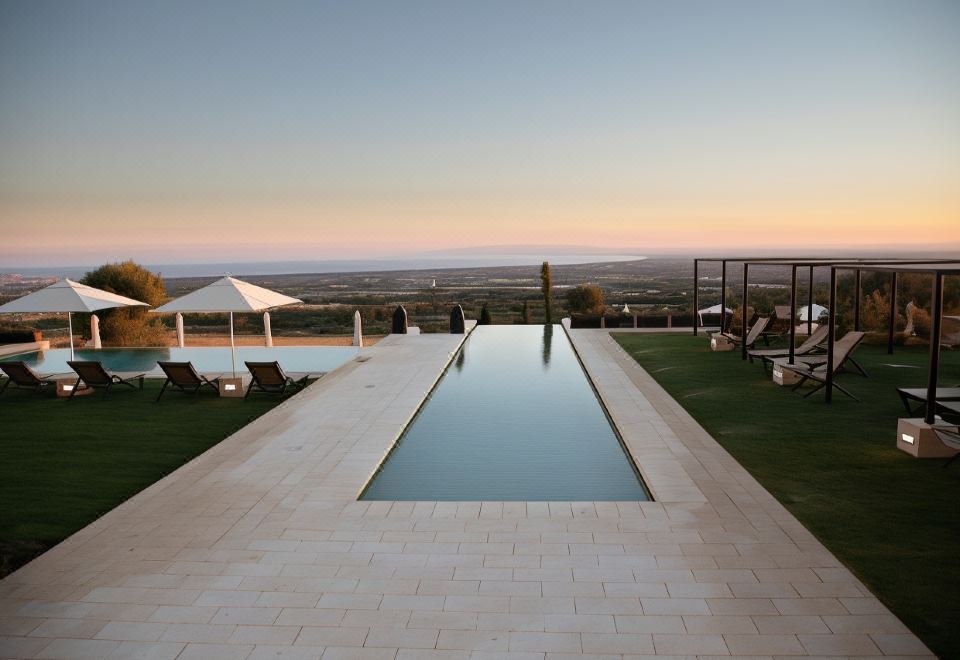 a long , empty pool is surrounded by lounge chairs and a view of the ocean at Masseria Amastuola Wine Resort
