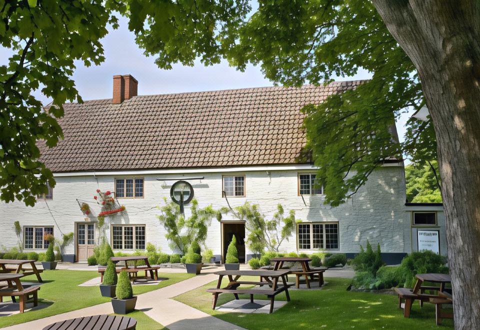 a large white house with a brown roof , surrounded by green grass and trees , as well as outdoor dining tables and benches at The Orange Tree Thornham