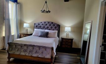 a bedroom with a large bed , two nightstands , and a mirror on the wall , illuminated by hanging lights at The Inn at Stone Mill