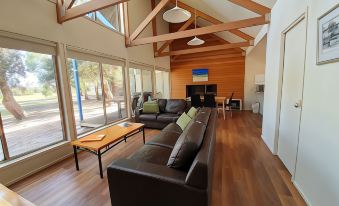 a spacious living room with a large flat - screen tv mounted on the wall , surrounded by couches and chairs at Waterfront Retreat at Wattle Point