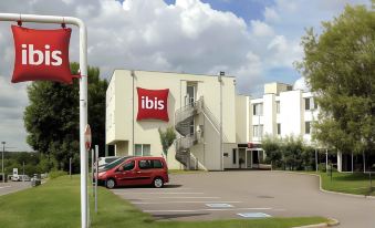 "a car parked in front of a building with a red banner that says "" ibis ""." at Ibis Longwy Mexy