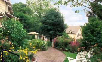 a beautiful garden with various flowers , trees , and a brick path leading to a house at The Inn at Montchanin Village