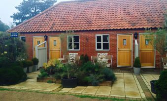 a red brick building with yellow doors and a gray roof , surrounded by plants and benches at The Orange Tree Thornham
