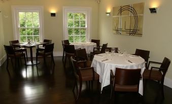 a well - lit dining room with wooden floors , white walls , and several round tables set for a meal at Flynns of Termonfeckin Boutique Hotel