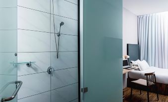 a modern bathroom with white tiles and a glass shower door , as well as a bedroom with a bed and desk at Hako Hotel (Mount Austin)