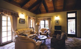 a cozy living room with wooden ceiling , beige furniture , and large windows , featuring comfortable seating arrangements at Holberry House