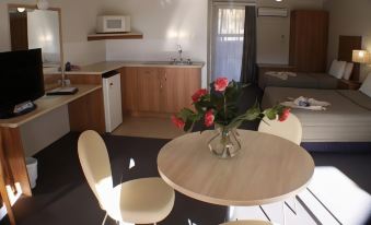 a modern kitchen and dining area with a wooden table , white chairs , and a vase of flowers at Fairway Motor Inn