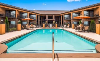 a large swimming pool with a metal ladder and lounge chairs is surrounded by an orange building at Aiden by Best Western @ Warm Springs Hotel and Event Center