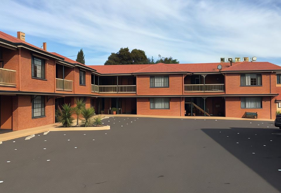 a large parking lot with multiple red - brick buildings in the background , under a clear blue sky at Poet's Recall Motel