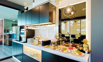 a well - lit kitchen with black cabinets , white countertops , and various food items displayed on the counter at The Living Hotel SamutPrakan