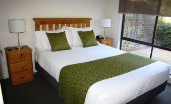 a neatly made bed with a wooden headboard and green pillows is shown in a bedroom at A-Line Holiday Park