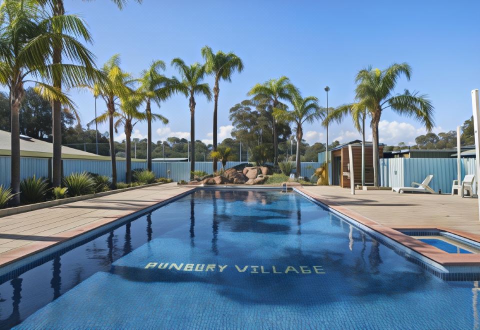 "a large swimming pool with a sign that reads "" punchy village "" is surrounded by palm trees" at Discovery Parks - Bunbury