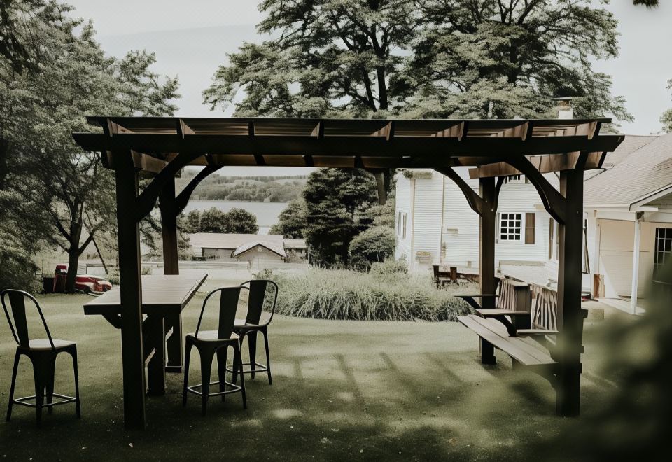 a wooden pergola with a table and chairs under it , overlooking a green lawn and trees at The Bond 1835