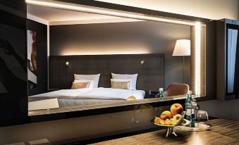 a modern hotel room with a large bed , wooden desk , and a tray of fruit on the table at Ginn Hotel Berlin Potsdam