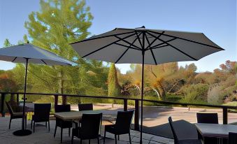 a patio with umbrellas , chairs , and tables set up for outdoor dining , surrounded by trees at Lyndoch Hill