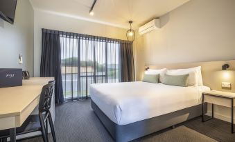 a modern hotel room with a large bed , white bedding , and a balcony offering views of the lake at Nightcap at Pymble Hotel