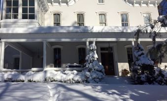 a white house with snow on the ground and trees in front of it , surrounded by snow at Susquehanna Manor Inn
