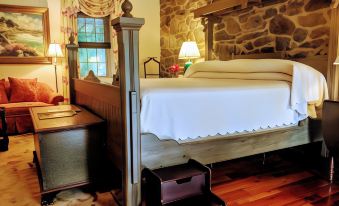 a bedroom with a bed , wooden nightstand , and a stone wall features a white blanket on the bed and a bedside table with a lamp at The Inn at Montchanin Village