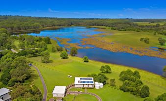 a large , lush green field with a small building and a body of water in the background at Narangba Motel (Formerly Brisbane North B&B and Winery)