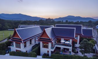 a large , two - story house with red roofs and white walls is surrounded by trees and mountains at Mae Rim Grace