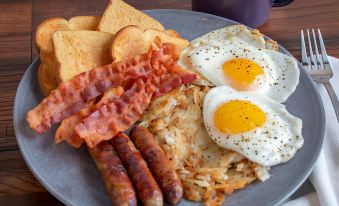 a plate of breakfast food , including bacon , eggs , toast , and sausage , is displayed on a wooden table at Hotel Valentino