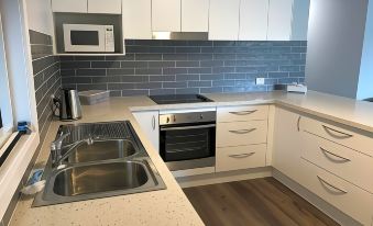 a modern kitchen with white cabinets and stainless steel appliances , including a sink , oven , and microwave at Ulladulla Motel