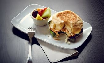 a white plate with a sandwich and a bowl of fruit on it , accompanied by a fork at Sonesta Select Columbia