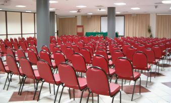 a large conference room filled with rows of red chairs and a podium at the front at Hotel Astoria