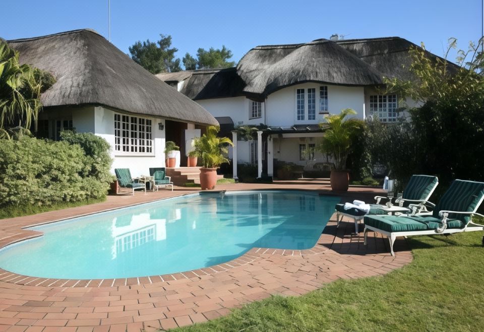 a beautiful white house with a thatched roof , surrounded by lush green grass and a swimming pool at Summerhill Guest Estate