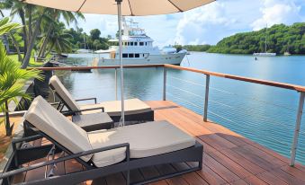 a wooden deck overlooking a body of water , with several lounge chairs and an umbrella placed on the deck at Novotel Suva Lami Bay